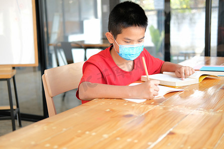 戴着口罩学习写笔记做作业的男孩学生。
