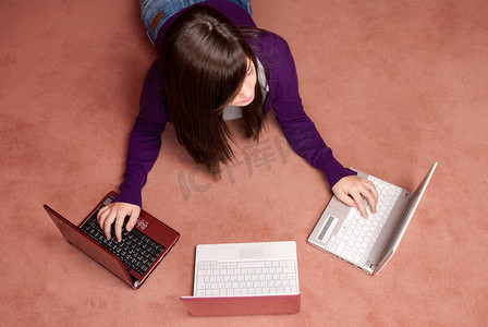 一心向党摄影照片_年轻女性一心多用，三台笔记本电脑躺在地板上