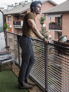 站立在阳台的英俊的深色头发的年轻人