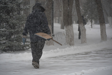 市政服务的一名工作人员带着雪铲在暴风雨、暴风雪或冬季降雪中在城市的恶劣天气中沿着道路行走。北方的极端冬季天气条件。