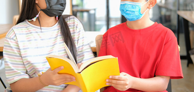 儿童口罩摄影照片_戴口罩的男孩女孩学生在图书馆读书。