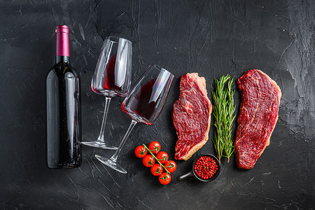 生的 picanha 牛排配调味料和香草，靠近瓶子和一杯红酒，在黑色质感的桌面视图上。