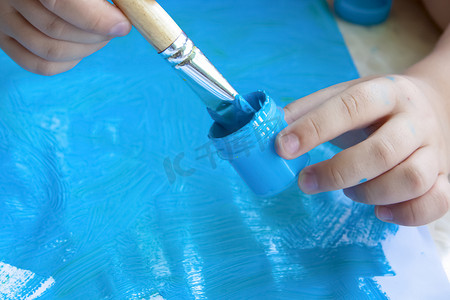 一个孩子的手拿着画笔，将画笔浸入颜料中。