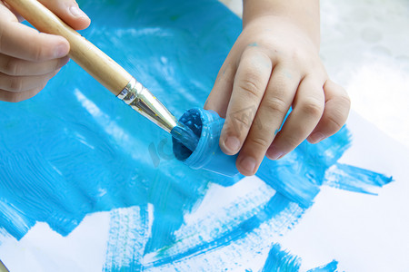 拿笔画画摄影照片_一个孩子的手拿着画笔，将画笔浸入颜料中。