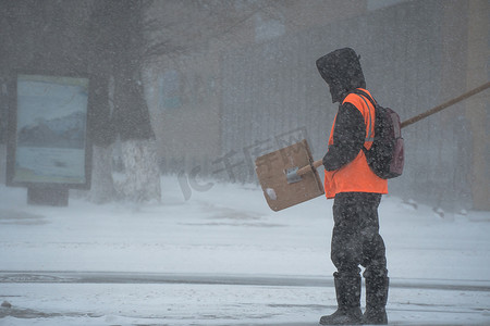 市政服务的一名工作人员带着雪铲在暴风雨、暴风雪或冬季降雪中在城市的恶劣天气中沿着道路行走。北方的极端冬季天气条件。