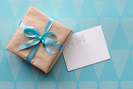 用牛皮纸包裹的礼品盒，蓝色背景上有蓝色丝带，并附有贺卡。