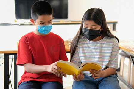 戴口罩的男孩女孩学生在图书馆读书。