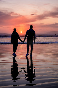 一对中年男女在加拿大托菲诺温哥华岛的海滩上看日落，海滩上美丽的日落，天空中有粉紫色