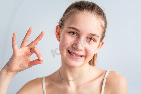 十几岁的女孩在牙齿矫正括号中微笑，显示出 OK 的手势。