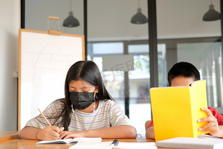 女孩男孩学生戴着口罩学习写笔记做作业。