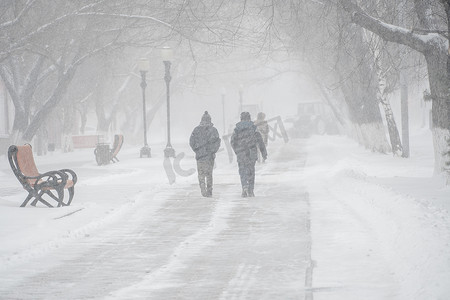 一条积雪覆盖的道路，冬天在城市的恶劣天气下，人们在暴风雪、暴风雪或降雪中。北方的极端冬季天气条件。人们在大雪中穿过街道
