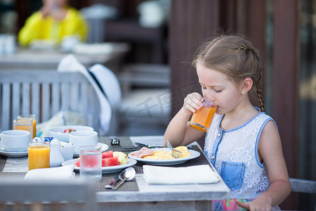 苹果早餐摄影照片_可爱的小女孩在户外咖啡馆喝苹果汁吃早餐