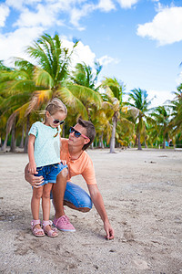 家庭度假摄影照片_海滩度假时，年轻爸爸和可爱的女儿在棕榈林里