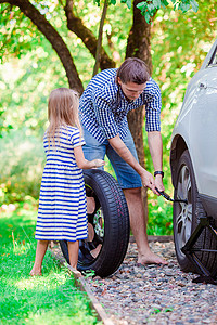 可爱的小女孩在美丽的夏日帮父亲在户外更换车轮