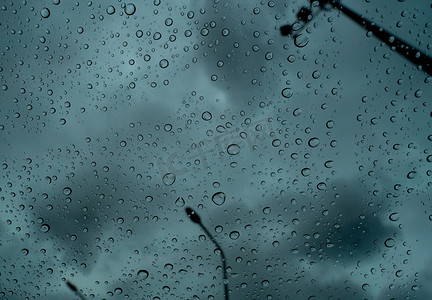 透明玻璃上的雨滴模糊了黑暗的暴风雨天空，