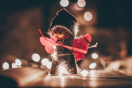 圣诞花环摄影照片_木制天使圣诞花环立在一本书上，背景是一个 LED 花环。