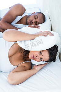 不安的妻子在打呼噜的丈夫旁边睡觉