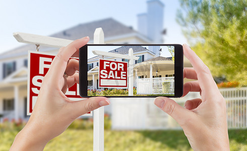 女性手拿着智能手机显示待售房地产标志和房子的照片。