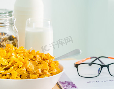 一碗带勺子的麦片和一杯牛奶放在靠近糖尿病教科书和眼镜的木桌上。