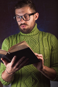 留着胡子的年轻英俊男子穿着绿色针织毛衣看书。