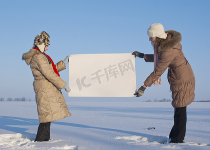 冬天海报摄影照片_在冬天雪地里拿着白色海报的女孩