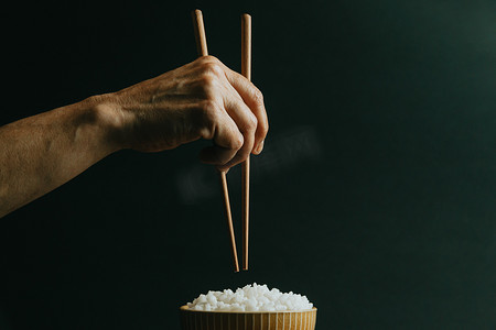 极简主义的老手在一碗米饭上抓着日本筷子，概念是在黑色背景下用电影色调拍摄的