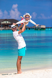 家庭度假摄影照片_热带海滩度假期间可爱的小女孩和快乐的父亲