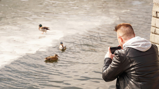 一个年轻人在给水里的鸭子拍照。
