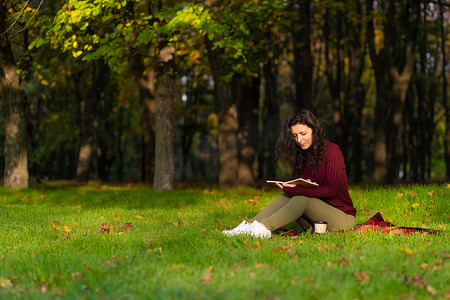 一个可爱的女孩在绿色的草坪上读书，喝咖啡