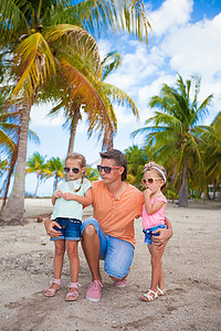 海滩度假时，年轻的爸爸和可爱的女儿们在棕榈林里