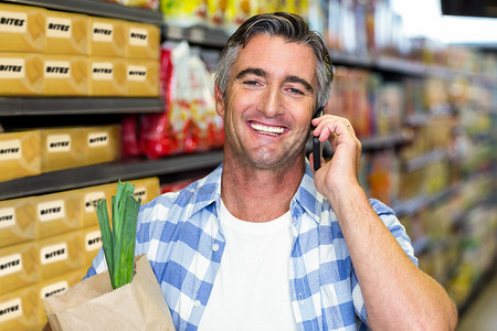 微笑的男人拿着食品袋打电话