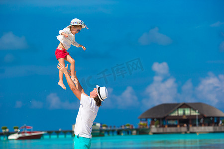 家庭度假摄影照片_热带海滩度假期间可爱的小女孩和快乐的爸爸