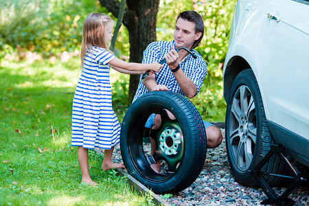 可爱三角形摄影照片_可爱的小女孩在美丽的夏日帮父亲在户外更换车轮