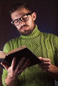 留着胡子的年轻英俊男子穿着绿色针织毛衣看书。