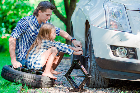可爱的小女孩坐在轮胎上，在美丽的夏日帮父亲在户外换车轮