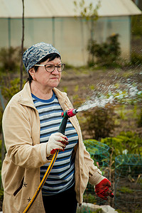 草坪和人摄影照片_园艺和人的概念 — 快乐的老年女性在夏天用花园软管浇灌草坪