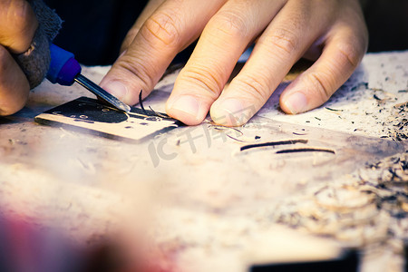 艺术创作摄影照片_工匠的手用雕刻工具在木工桌工作台上雕刻，在艺术课上学习工匠专业。