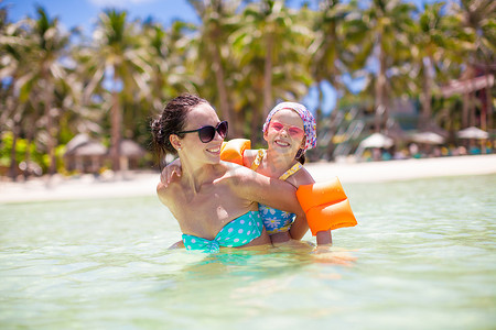 热带海滩度假期间可爱的小女孩和快乐的妈妈