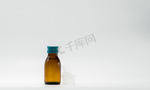 止咳摄影照片_琥珀瓶中的止咳糖浆，带有空白标签和塑料量杯，白色背景中的茶匙