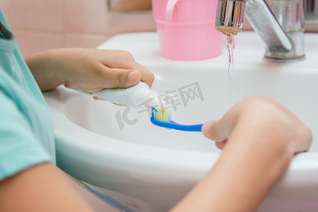 黑茶牙膏摄影照片_孩子从牙刷上的管子里挤出牙膏
