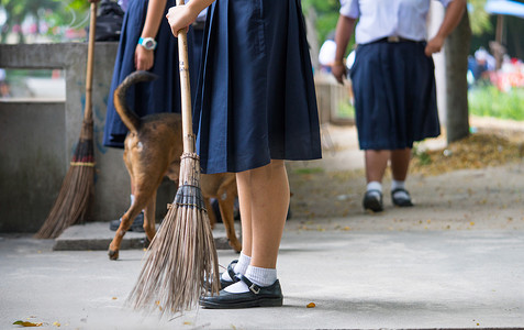 女学生一边遛狗一边用扫帚帮忙扫水泥地