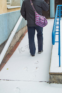 爬坡道摄影照片_一位白发苍苍的老人在积雪覆盖的残疾人坡道上艰难攀爬，在雪中留下痕迹