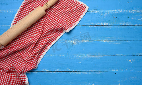 蓝色别针摄影照片_木质蓝色背景上的罗林夫别针和折叠的红白棉质厨房餐巾，