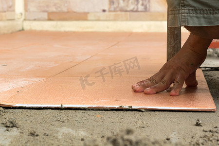 贴瓷砖摄影照片_男建筑工人在家贴瓷砖，瓷砖地板粘合剂 r