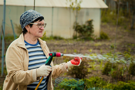 草坪和人摄影照片_园艺和人的概念 — 快乐的老年女性在夏天用花园软管浇灌草坪
