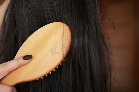 女手握着长发黑假发，梳着木梳