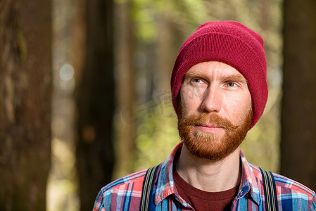 森林里一个戴着红帽子的大胡子男子沉思的画像