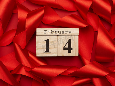 2.14摄影照片_红色背景上的日期为 2 月 14 日的木制日历，上面有一条扭曲的红丝带