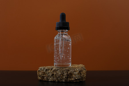 应用要素摄影照片_棕色背景下石头和黑桌上透明瓶中的抗衰老或保湿皮肤血清