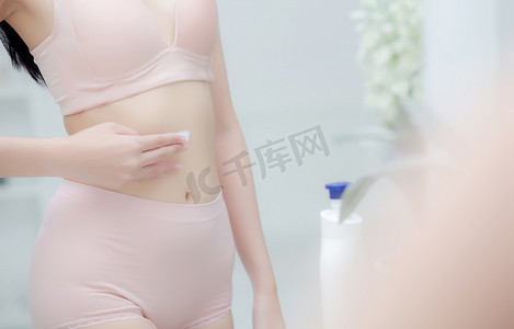 美丽的年轻亚洲女性穿着内衣照镜子，在腹部涂抹奶油和乳液，美女节食和减肥苗条，应用信息身体护理、治疗和带保湿霜的化妆品。